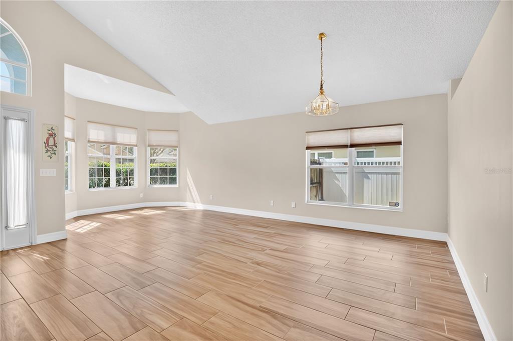 An empty living room features light wood-look tile flooring, vaulted ceilings, and several large windows — 13538 FORDWELL DRIVE, ORLANDO, FL