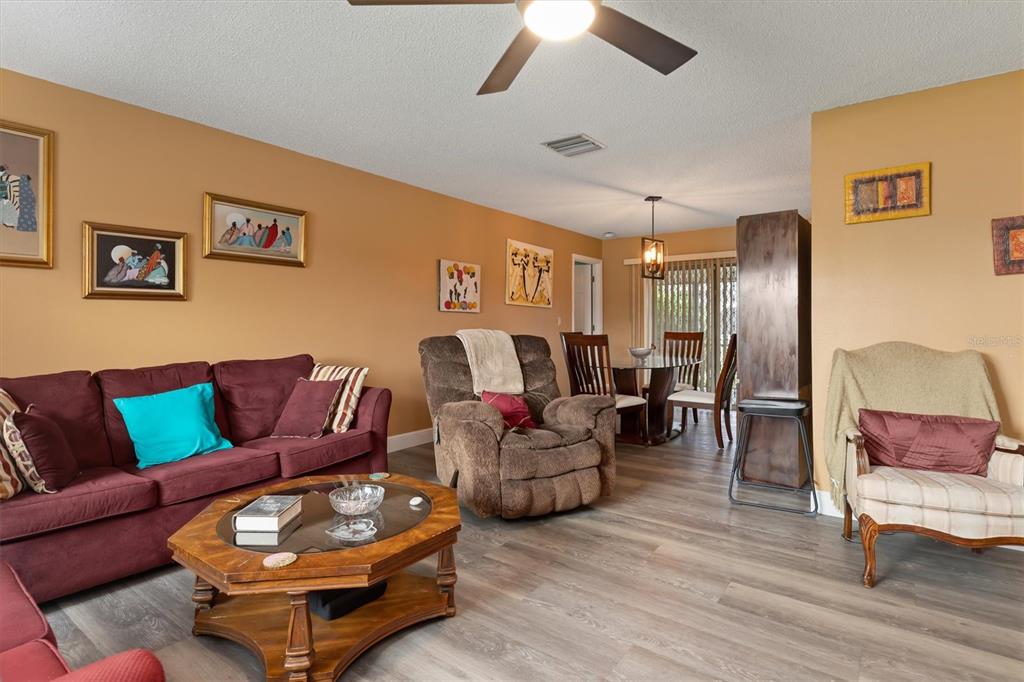 A living room with wood-look flooring, a maroon sofa, a brown recliner, and a dining area — 23226 MIDWAY BOULEVARD, PUNTA GORDA, FL