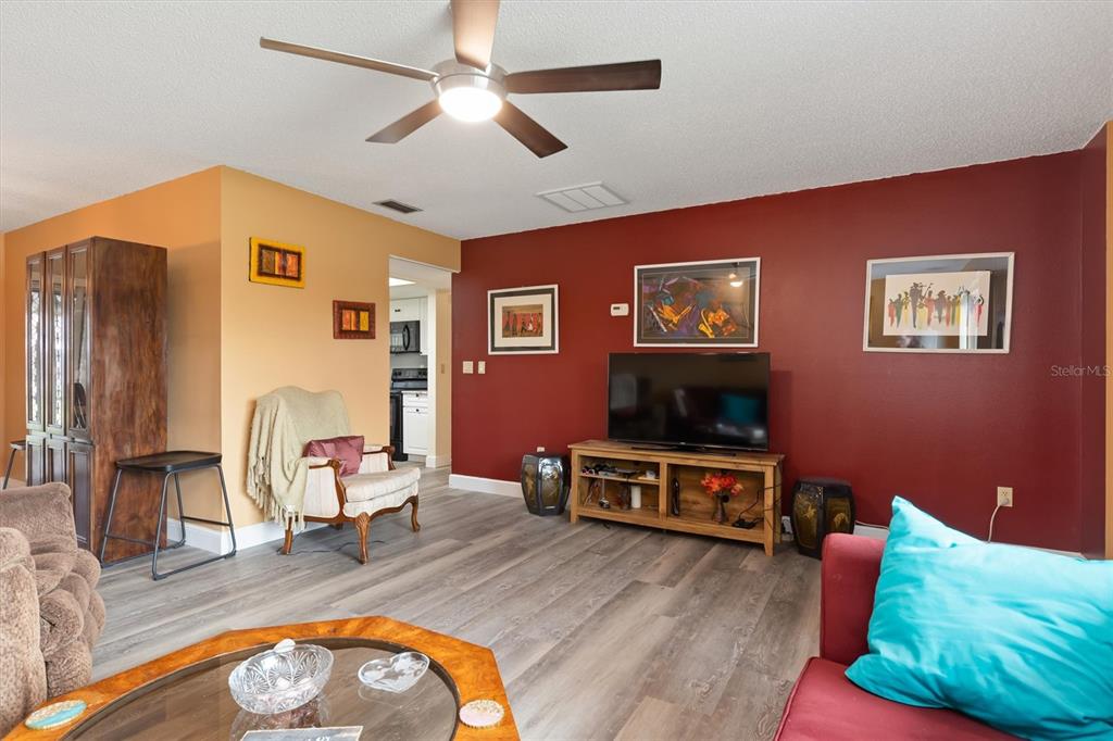 A living room features wood-look flooring, a ceiling fan, and a red accent wall — 23226 MIDWAY BOULEVARD, PUNTA GORDA, FL