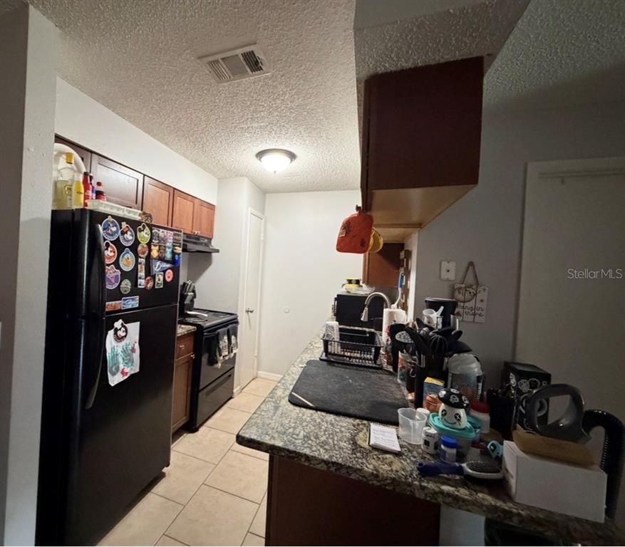 A kitchen features dark cabinets, black appliances, a granite countertop, and light-colored tile flooring — 237 RED MAPLE PLACE, BRANDON, FL