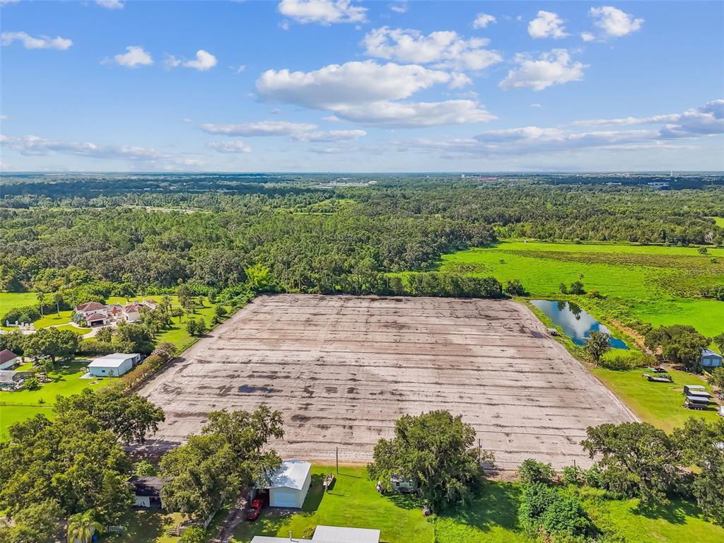 An aerial view shows a large, cleared rectangular dirt lot surrounded by trees and grass — 1715 W SAM ALLEN ROAD, PLANT CITY, FL