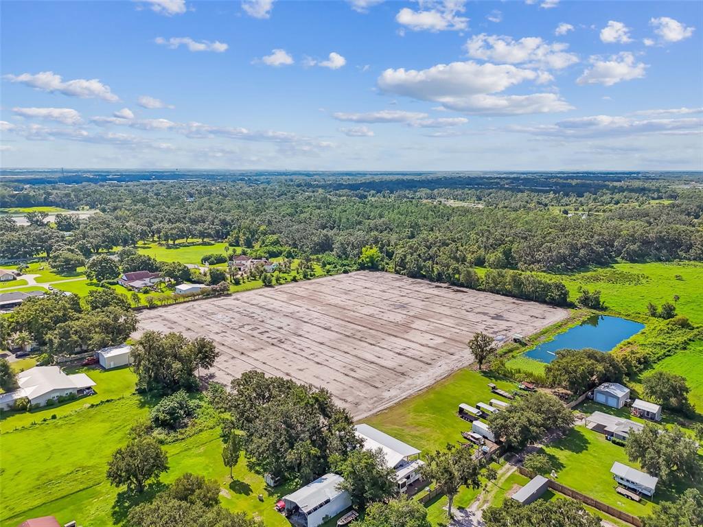 An aerial view shows a large, cleared rectangular dirt lot surrounded by trees and houses — 1715 W SAM ALLEN ROAD, PLANT CITY, FL