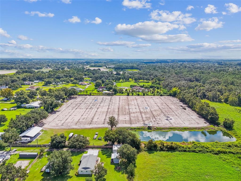 An aerial view shows a large, cleared rectangular lot adjacent to a pond and houses — 1715 W SAM ALLEN ROAD, PLANT CITY, FL