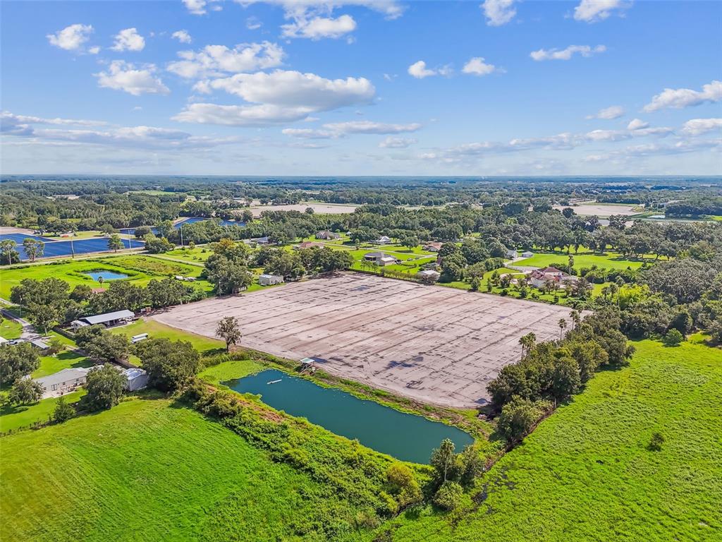 An aerial view shows a large cleared dirt lot next to a pond and trees — 1715 W SAM ALLEN ROAD, PLANT CITY, FL