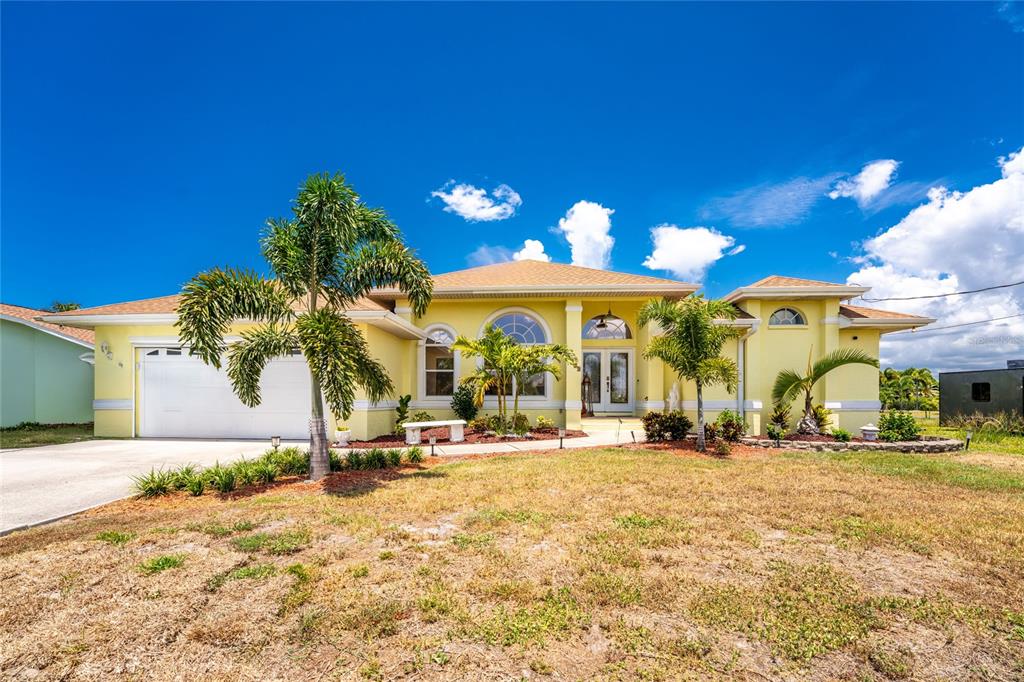 A yellow single-story house with a white garage and palm trees under a blue sky — 3015 WISTERIA PLACE, PUNTA GORDA, FL