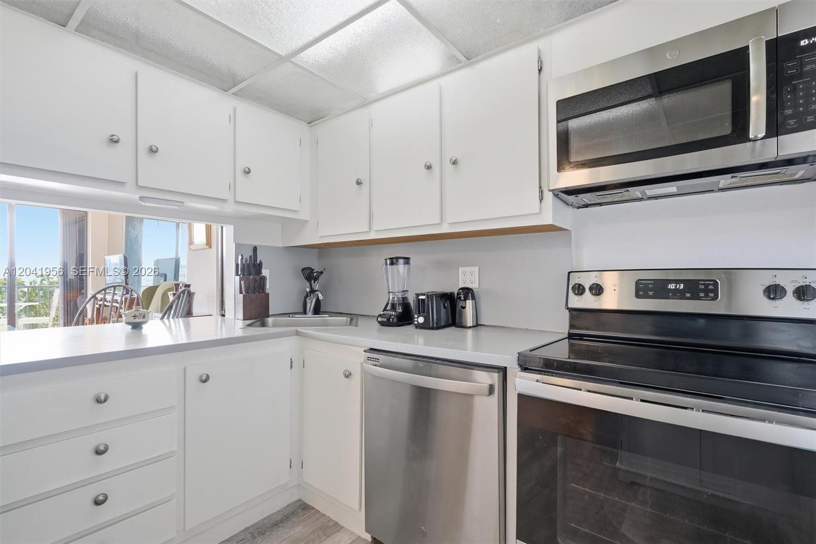 A kitchen features white cabinets, stainless steel appliances, and a view of a balcony — 1470 NE 123rd St # A609, North Miami FL 33161, NORTH MIAMI, FL