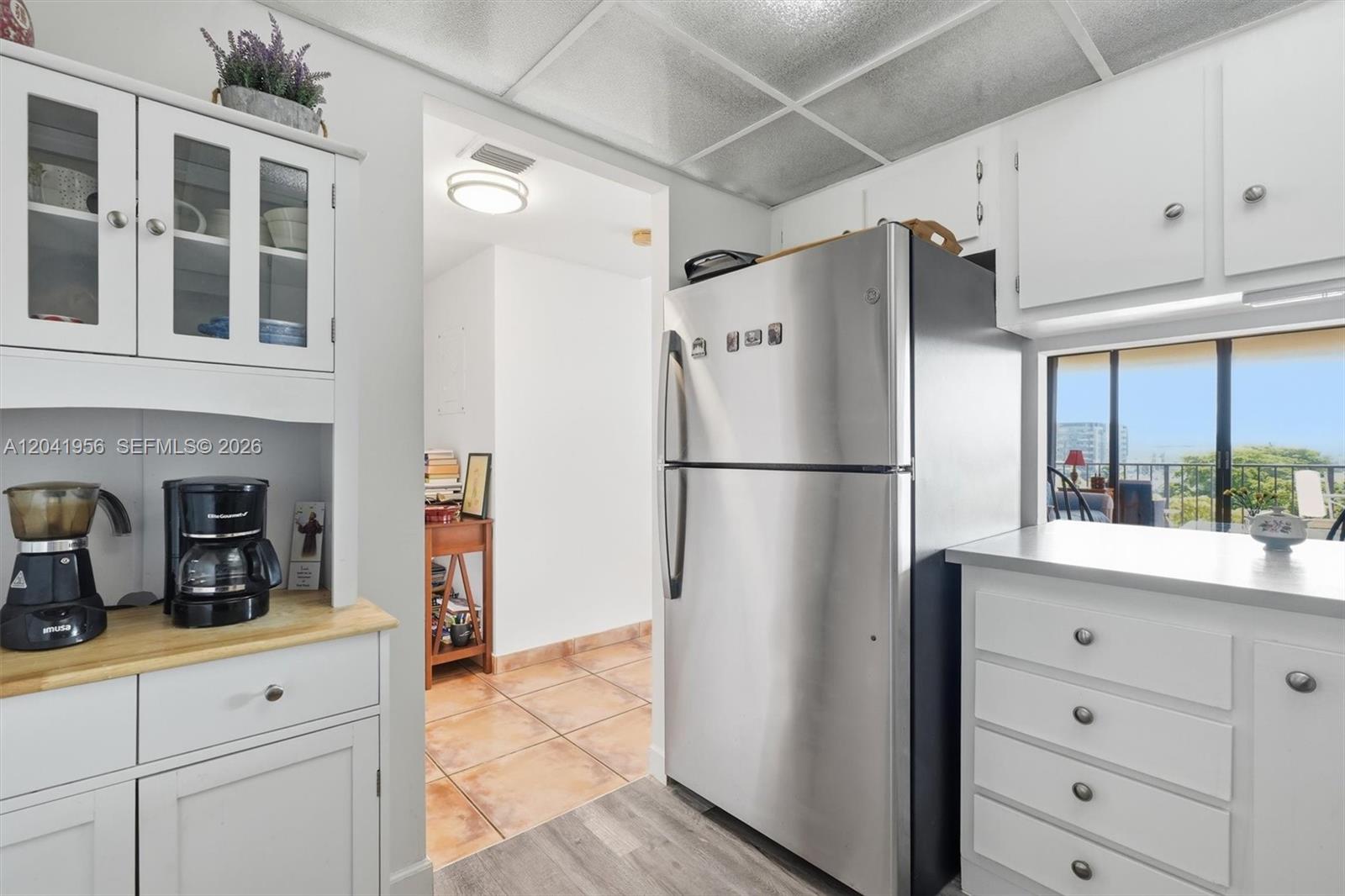 A kitchen features white cabinetry, a stainless steel refrigerator, and a view of a balcony — 1470 NE 123rd St # A609, North Miami FL 33161, NORTH MIAMI, FL