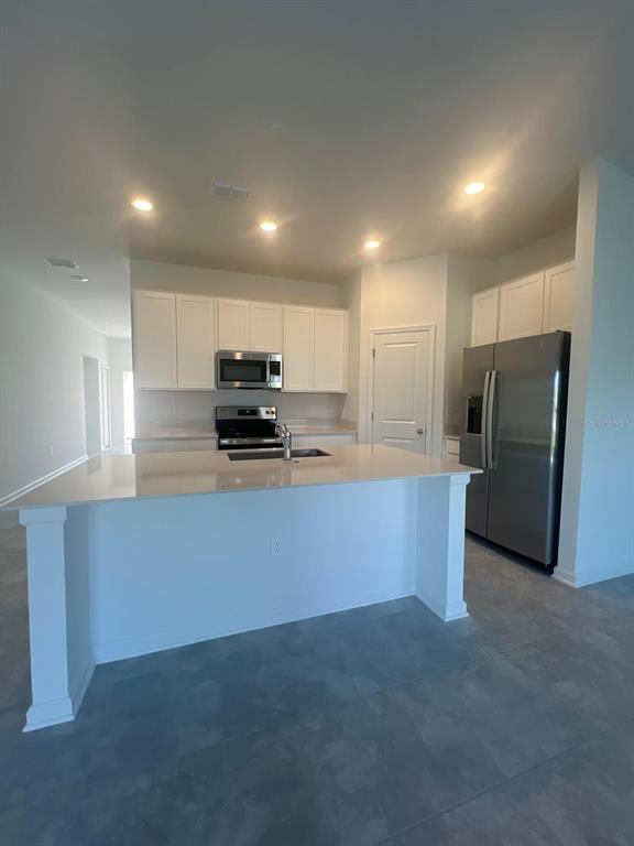 A kitchen features white cabinets, stainless steel appliances, a quartz island, and gray tile flooring — 413 CEDAR KEY STREET, DAVENPORT, FL