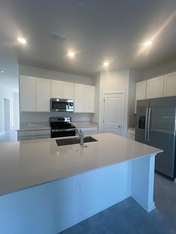 A modern kitchen features white cabinets, stainless steel appliances, and a large quartz-topped island — 413 CEDAR KEY STREET, DAVENPORT, FL
