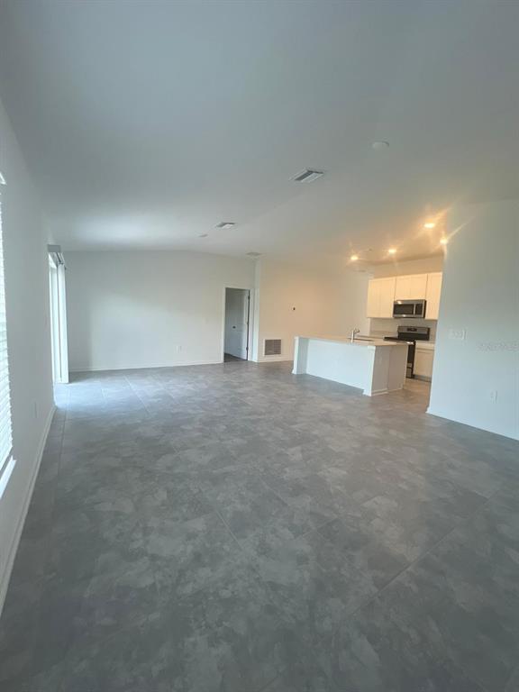 An open-concept living area features gray tile flooring and a kitchen with white cabinetry — 413 CEDAR KEY STREET, DAVENPORT, FL