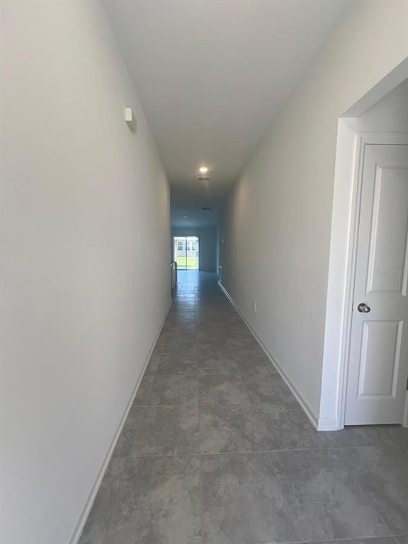 A long hallway with gray tile flooring leads toward a glass sliding door — 413 CEDAR KEY STREET, DAVENPORT, FL