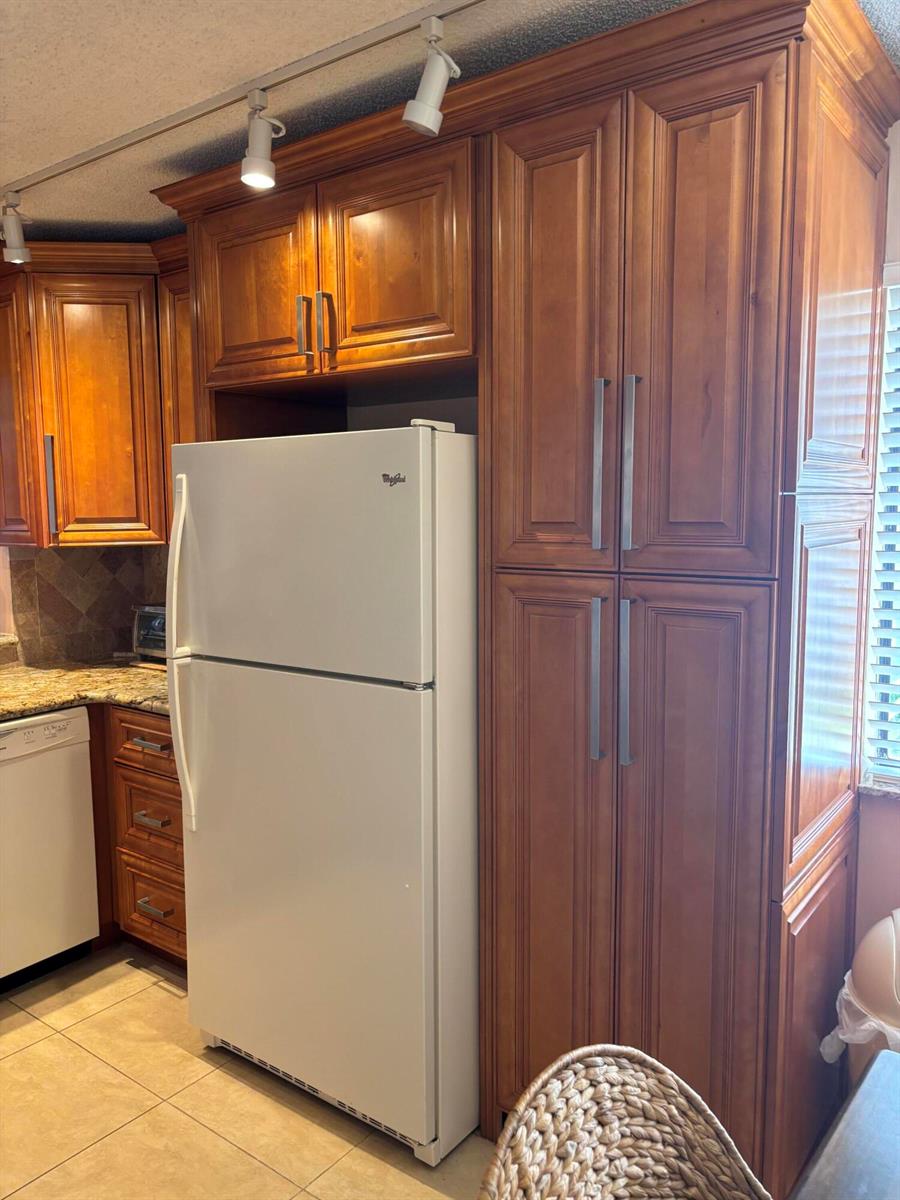 A white refrigerator is positioned between wooden kitchen cabinets in a tiled kitchen — 60 Pelican Pointe Drive # 1020, Delray Beach FL 33483, DELRAY BEACH, FL