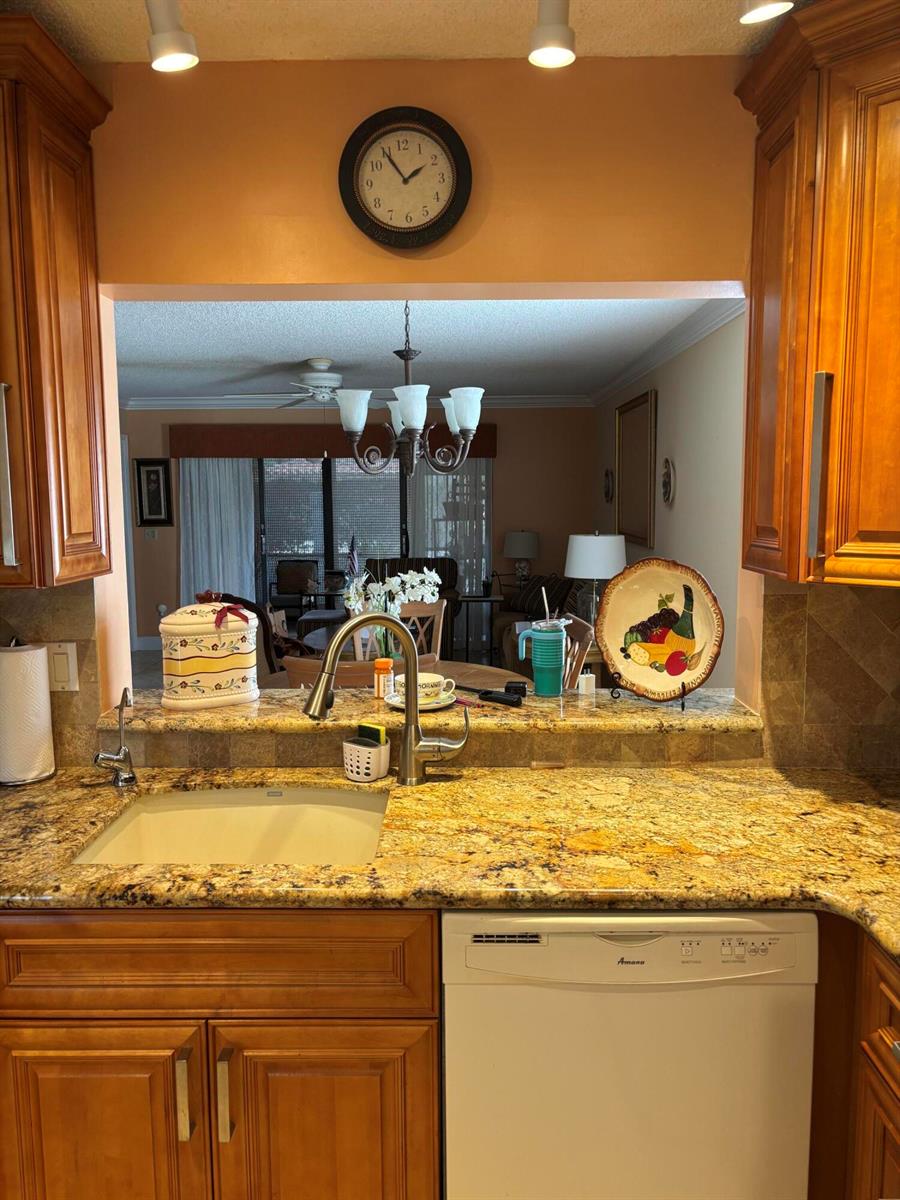 A kitchen features wood cabinets, granite countertops, a white sink, and a view into the living room — 60 Pelican Pointe Drive # 1020, Delray Beach FL 33483, DELRAY BEACH, FL