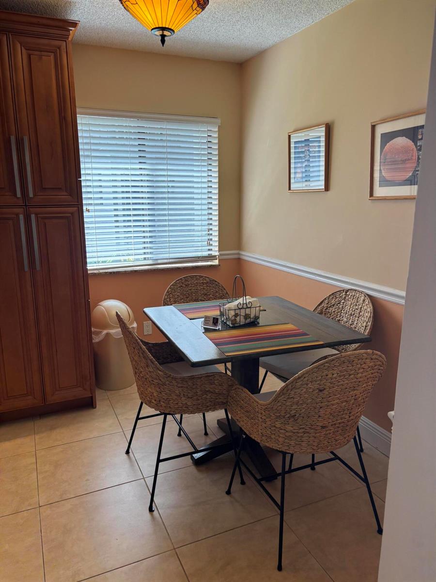 A dining nook features a square wooden table, four woven chairs, and a window — 60 Pelican Pointe Drive # 1020, Delray Beach FL 33483, DELRAY BEACH, FL
