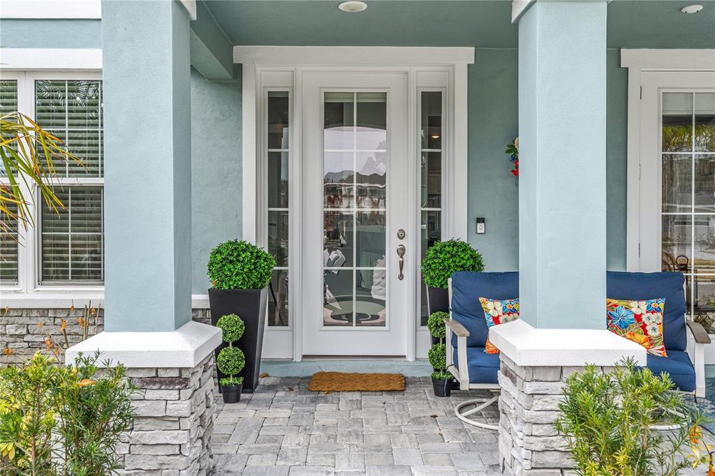 A front porch with a white glass-paneled door, stone columns, and blue patio furniture — 3102 MELETO BOULEVARD, NEW SMYRNA BEACH, FL