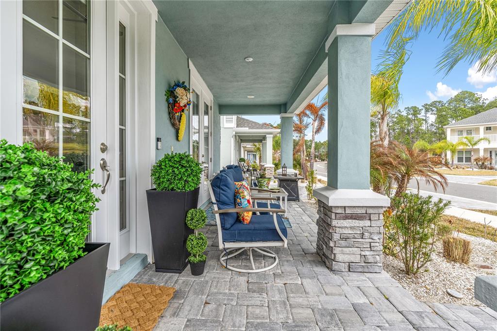 A covered front porch features stone-based columns, blue patio furniture, and potted greenery — 3102 MELETO BOULEVARD, NEW SMYRNA BEACH, FL