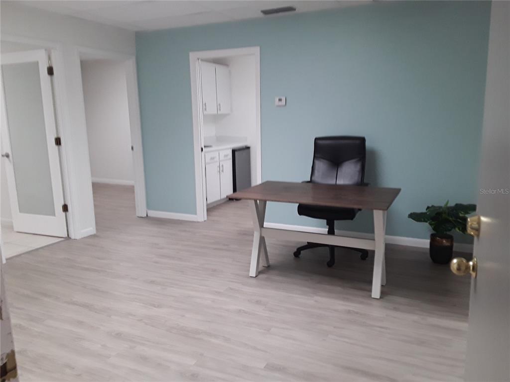 An office room features light blue walls, wood-look flooring, a desk, and a small kitchenette — 1310 N MAIN STREET, KISSIMMEE, FL