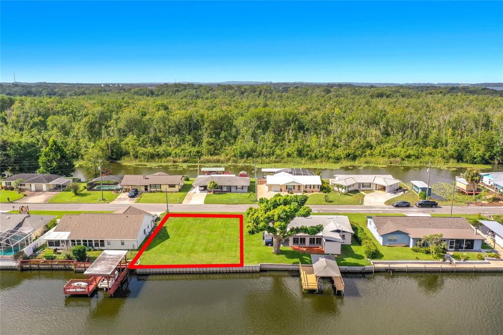 An aerial view shows a vacant, rectangular waterfront lot outlined in red between two houses — 13233 COUNTRY CLUB, TAVARES, FL