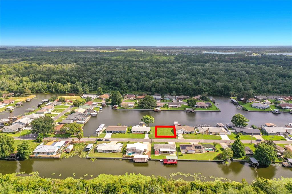 An aerial view shows a vacant residential lot highlighted in red along a canal — 13233 COUNTRY CLUB, TAVARES, FL