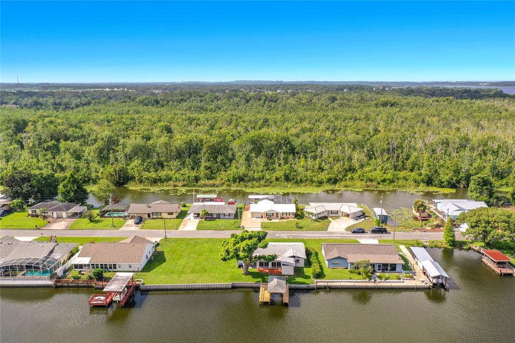 An aerial view shows waterfront houses with private docks along a canal bordering dense woods — 13233 COUNTRY CLUB, TAVARES, FL