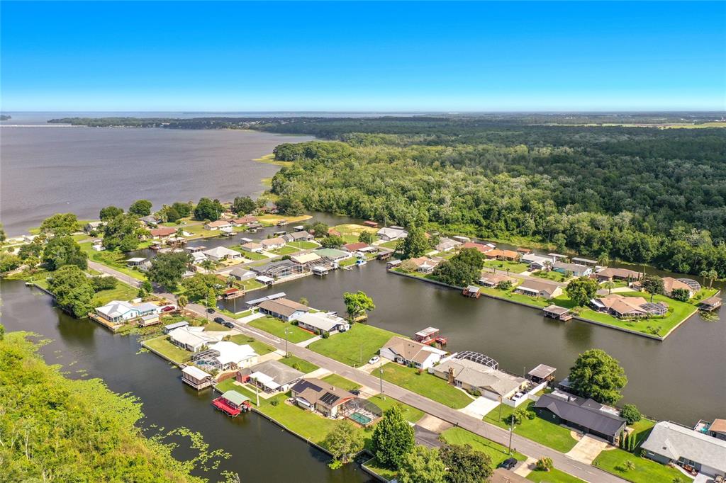 An aerial view shows a waterfront residential neighborhood with canals, docks, and surrounding dense forest — 13233 COUNTRY CLUB, TAVARES, FL