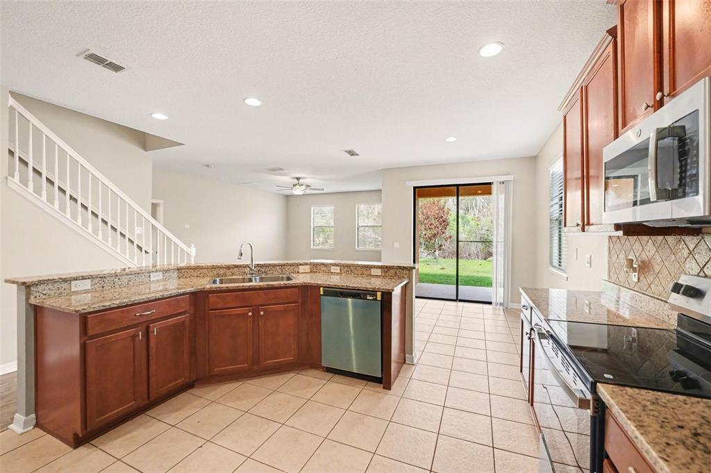 A kitchen with wood cabinets, granite countertops, and tile flooring overlooks a living area — 2727 EAGLE CLIFF DRIVE, KISSIMMEE, FL