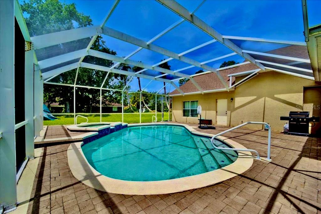 A screened-in patio features a swimming pool with an attached spa and paver decking — 24 LAKESIDE PLACE W, PALM COAST, FL
