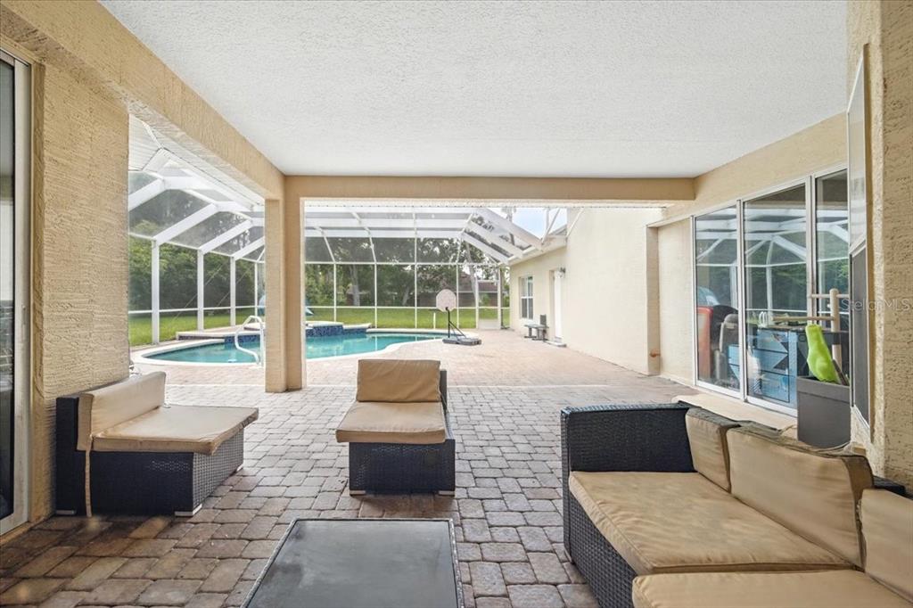 A covered patio features brick pavers, outdoor furniture, and a view of a screened pool — 24 LAKESIDE PLACE W, PALM COAST, FL