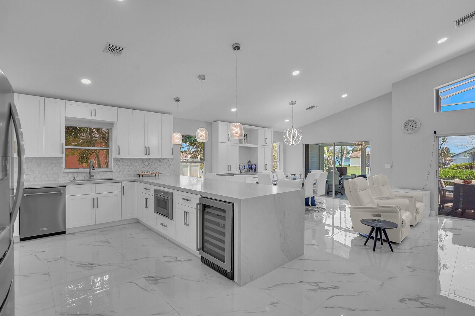 A modern white kitchen with a marble island, stainless steel appliances, and glossy tile floors — 7791 Great Glen Circle, Delray Beach FL 33446, DELRAY BEACH, FL