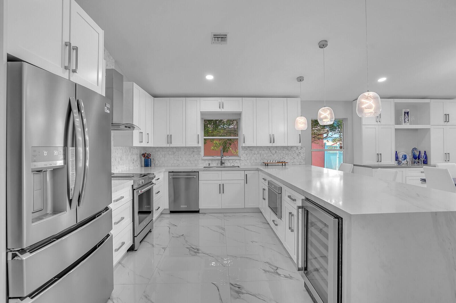 A modern white kitchen features stainless steel appliances, marble-look tile floors, and a large island — 7791 Great Glen Circle, Delray Beach FL 33446, DELRAY BEACH, FL