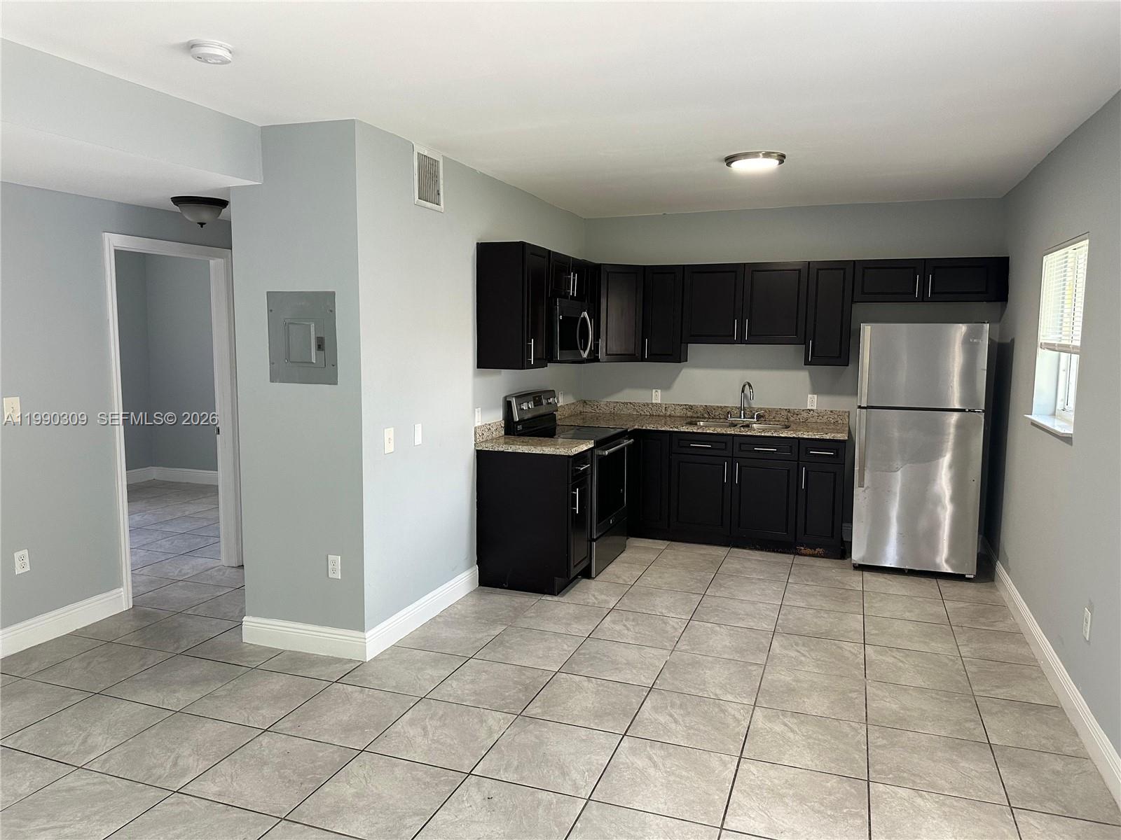 A kitchen features dark cabinets, stainless steel appliances, granite countertops, and light gray tile flooring — 6801 NW 2nd Ct # 6803, Miami FL 33150, MIAMI, FL