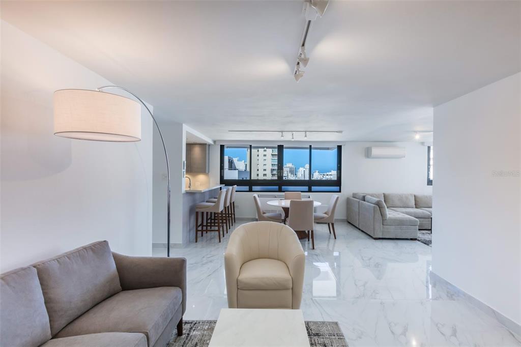 An open-concept living and dining area features white marble floors, modern furniture, and city views — 1485 ASHFORD AVENUE UNIT 16A, SAN JUAN, PR