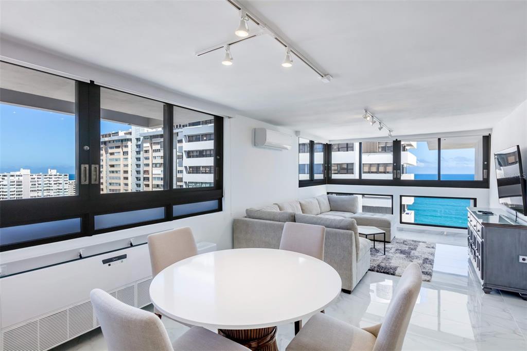 A bright living and dining area features white tile floors, modern furniture, and ocean views — 1485 ASHFORD AVENUE UNIT 16A, SAN JUAN, PR