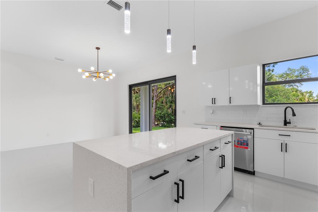 A modern kitchen features a white quartz island, white cabinetry, stainless steel appliances, and pendant lighting — 10070 FLAT RIVER ST, PORT CHARLOTTE, FL