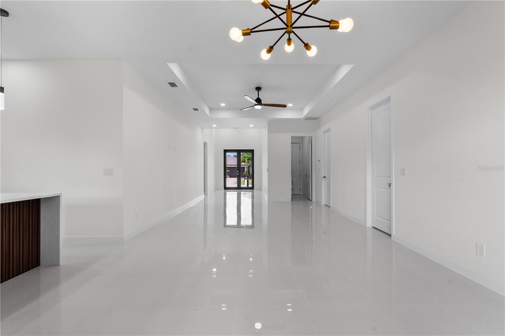 A bright, minimalist room features white tile floors, a tray ceiling, and a modern chandelier — 10070 FLAT RIVER ST, PORT CHARLOTTE, FL