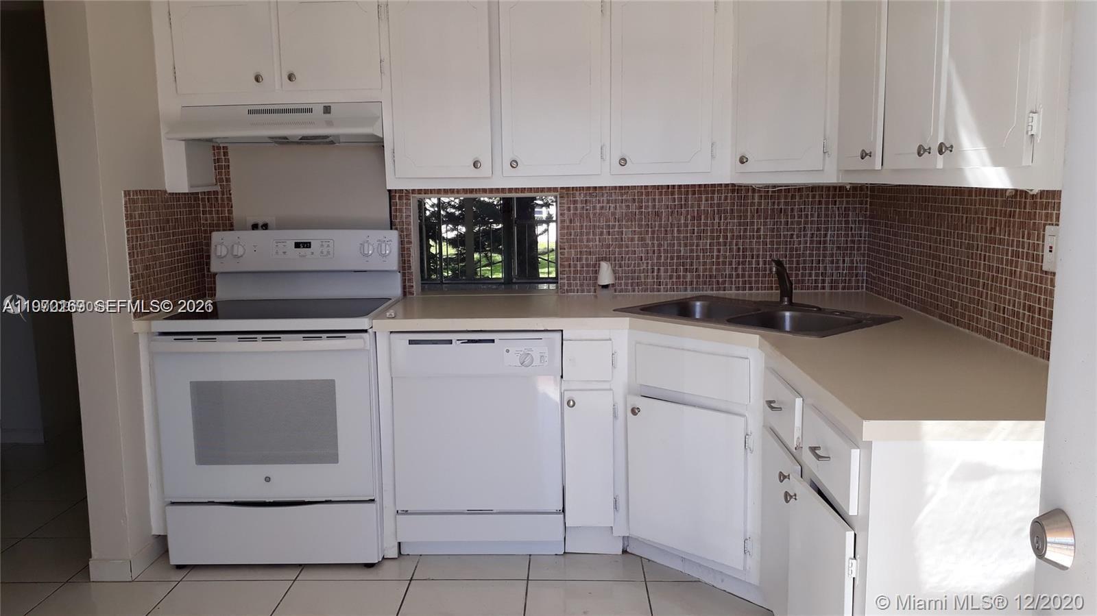 A kitchen features white cabinets, a white stove, a dishwasher, and a brown tiled backsplash — 1540 NE 191st St # 244, Miami FL 33179, MIAMI, FL