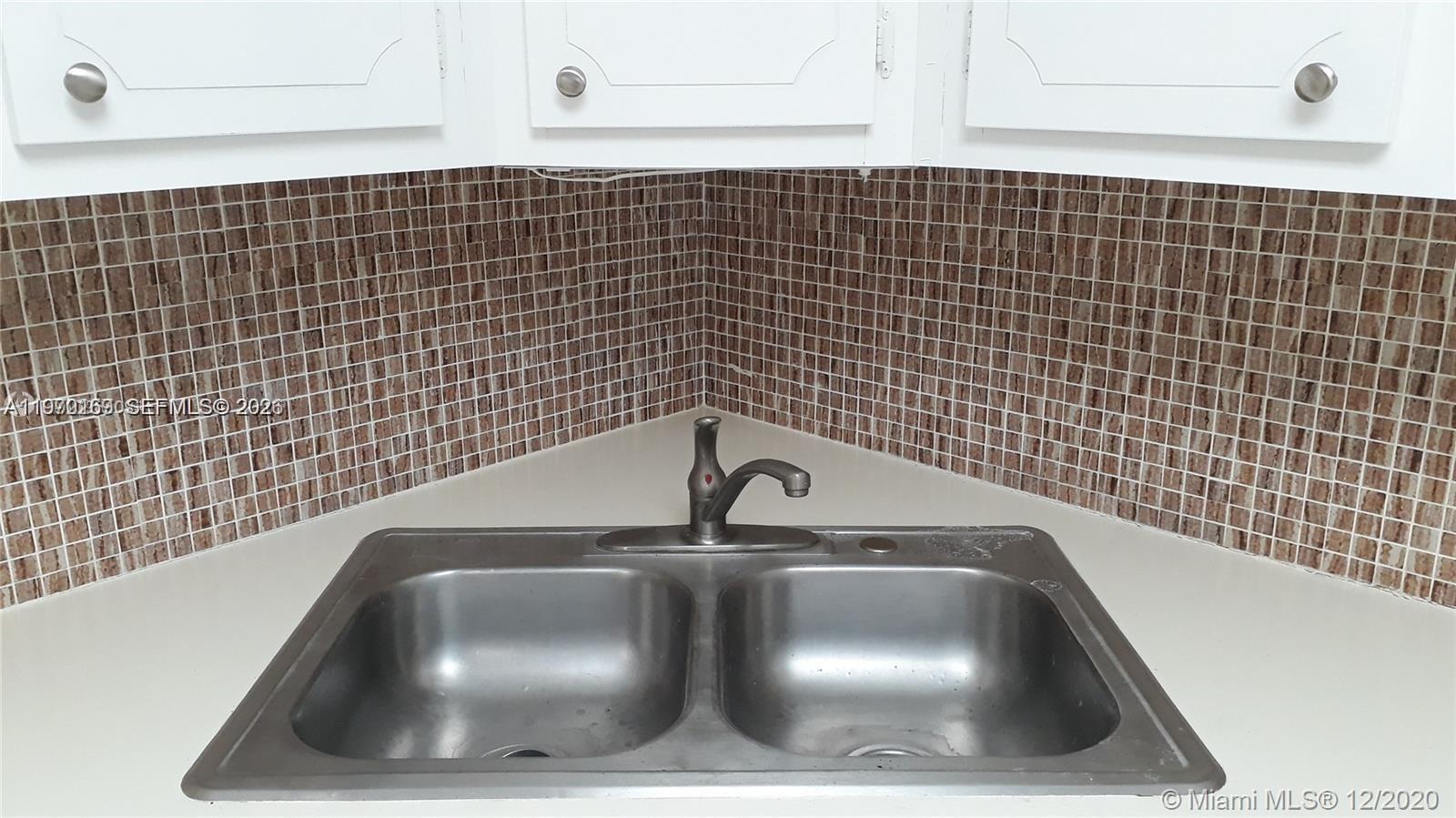 A double-basin stainless steel kitchen sink is set against a brown mosaic tile backsplash — 1540 NE 191st St # 244, Miami FL 33179, MIAMI, FL