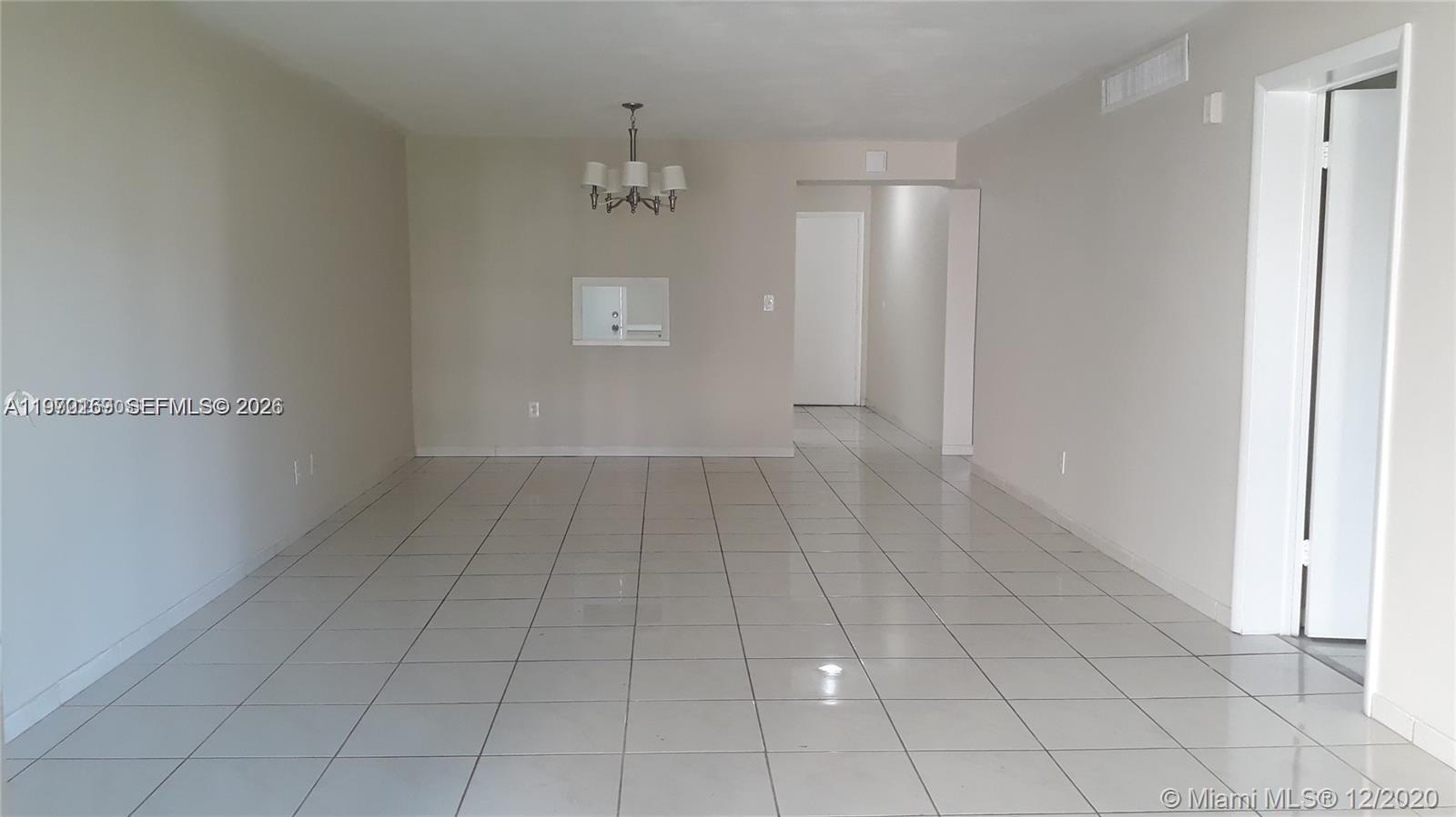 An empty room features light-colored floor tiles, beige walls, and a hanging light fixture — 1540 NE 191st St # 244, Miami FL 33179, MIAMI, FL