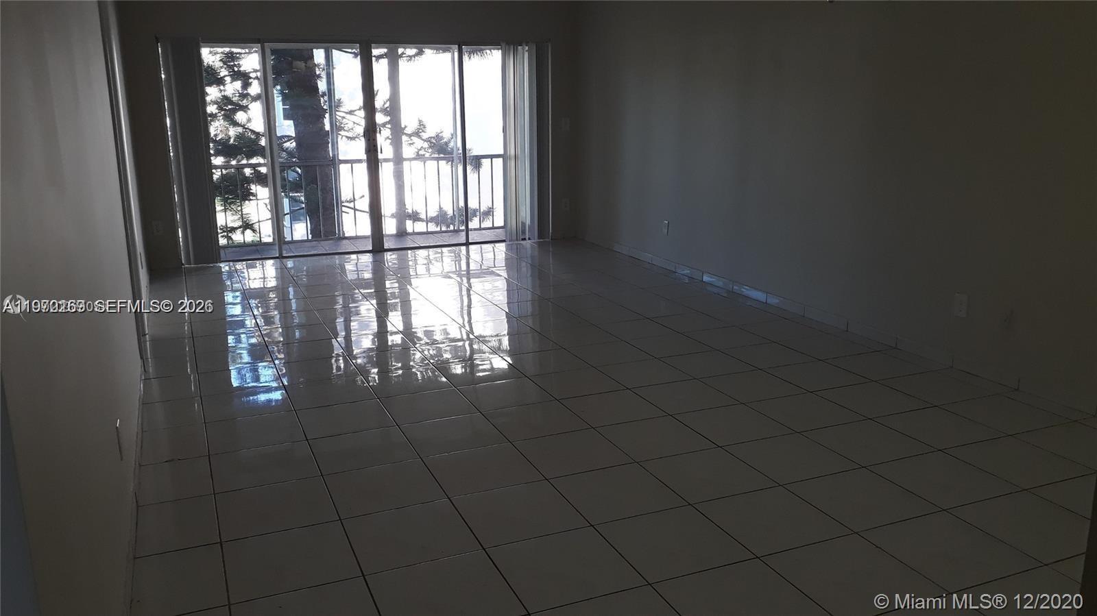 An empty room features white tiled floors and a large sliding glass door to a balcony — 1540 NE 191st St # 244, Miami FL 33179, MIAMI, FL