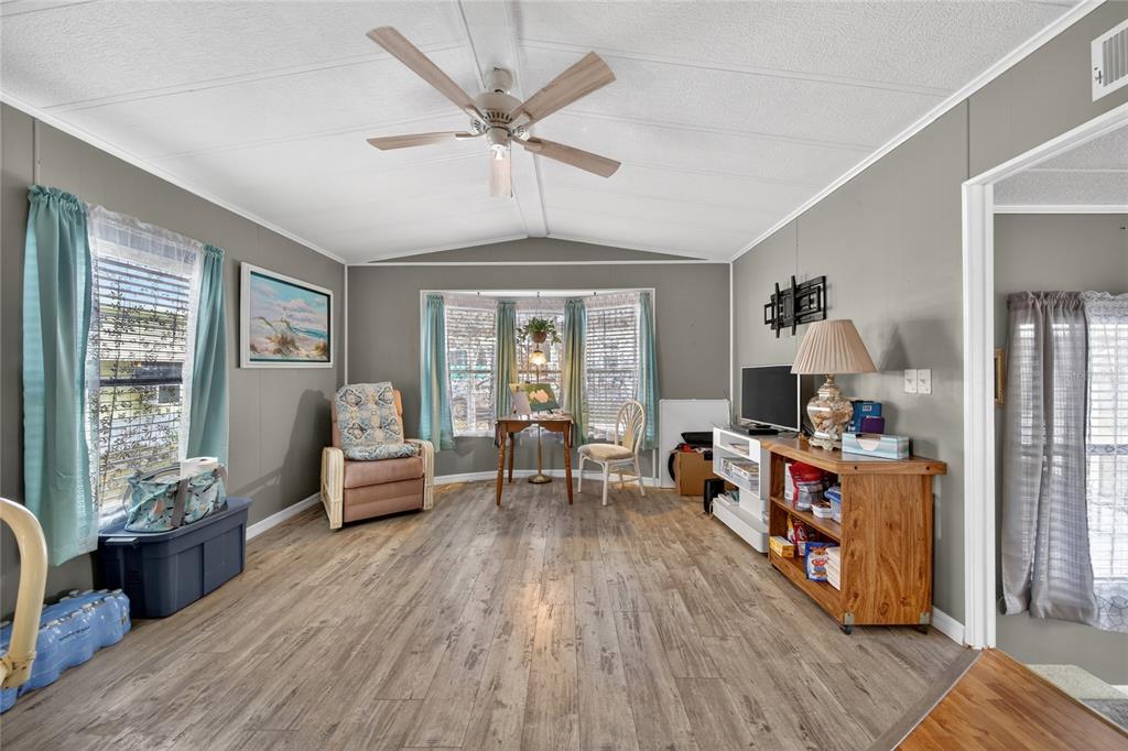A living room with gray walls, wood-look flooring, a ceiling fan, and a bay window — 251 PATTERSON ROAD UNIT D32, HAINES CITY, FL