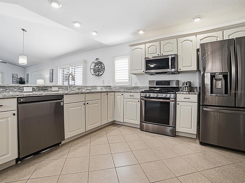 A kitchen features white cabinets, stainless steel appliances, granite countertops, and light tile flooring — 435 CARLISLE COURT, THE VILLAGES, FL