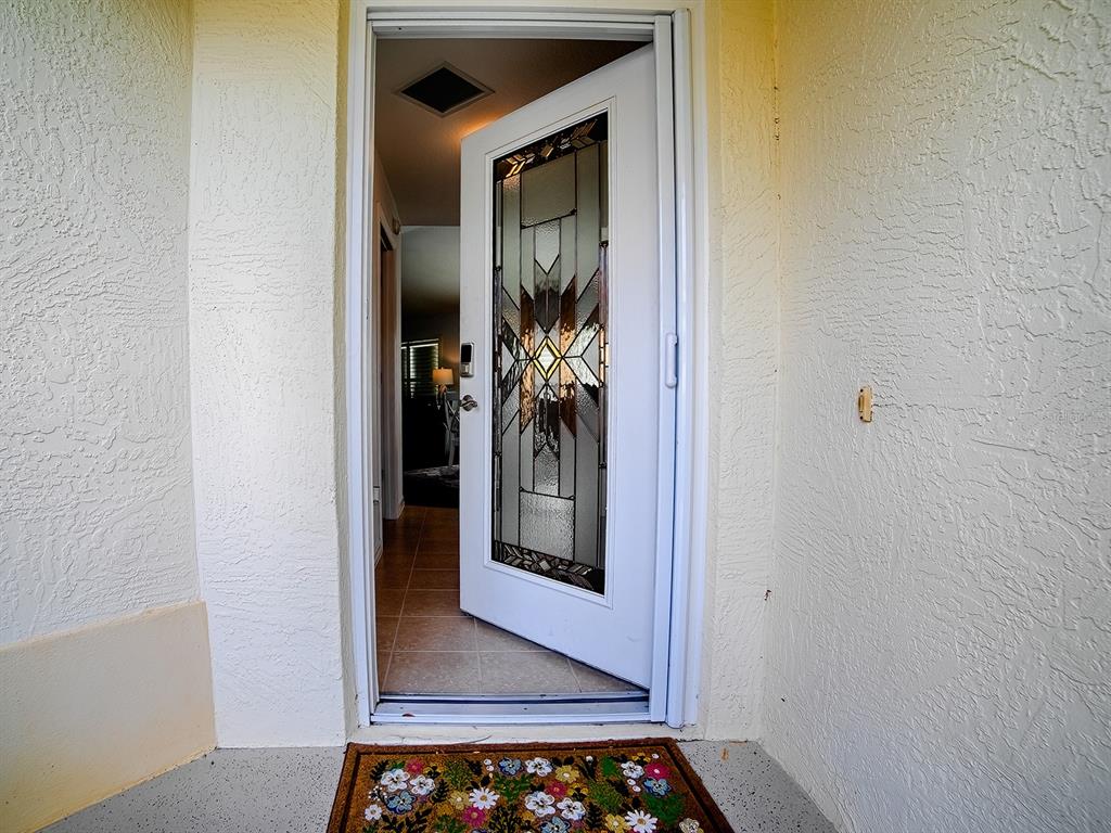An open white front door with a decorative glass insert leads into a tiled entryway — 435 CARLISLE COURT, THE VILLAGES, FL