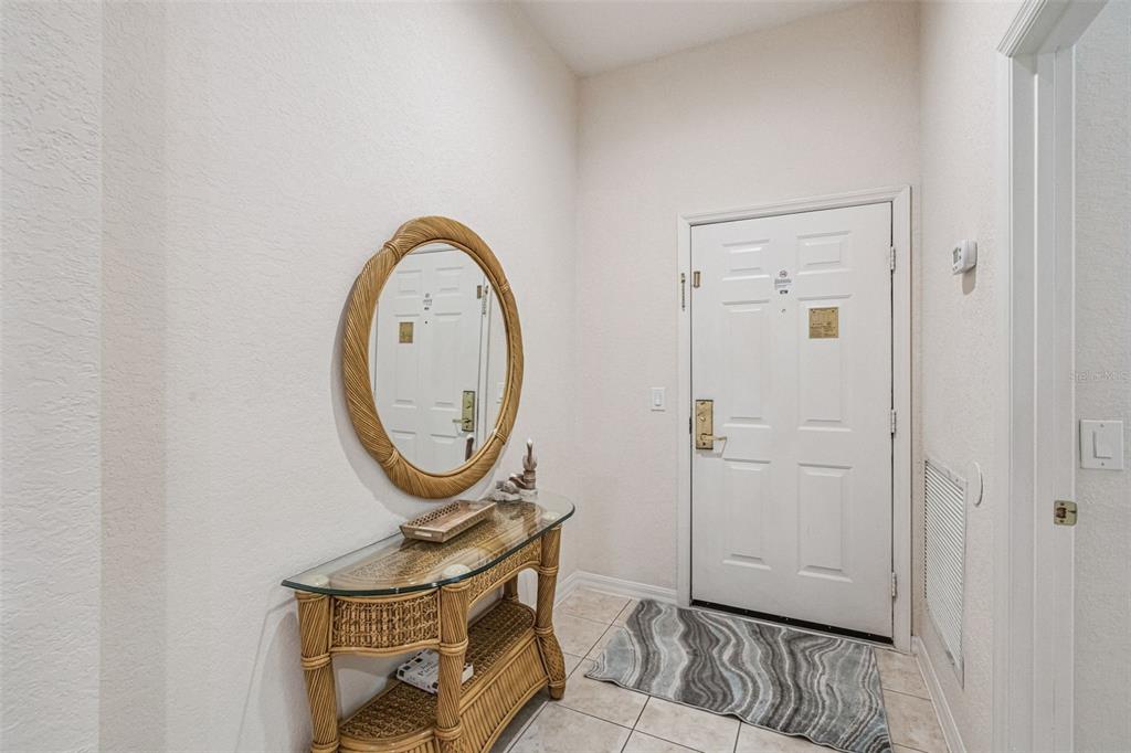 An entryway features a wicker console table, an oval mirror, and a white front door — 316 NEW PROVIDENCE PROMENADE, DAVENPORT, FL