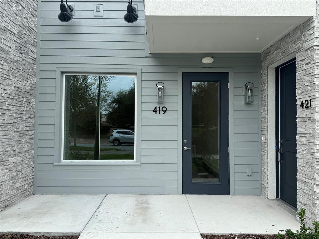 The exterior of a modern building features gray horizontal siding, stone accents, and two doors — 419 MIKE ROBERTO WAY, OVIEDO, FL