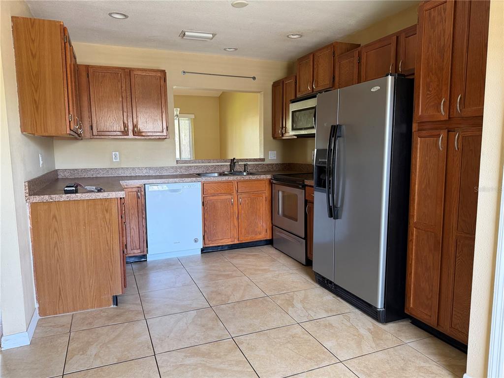 A kitchen features wood cabinets, stainless steel appliances, a white dishwasher, and tiled flooring — 600 NORTHERN WAY UNIT 702, WINTER SPRINGS, FL