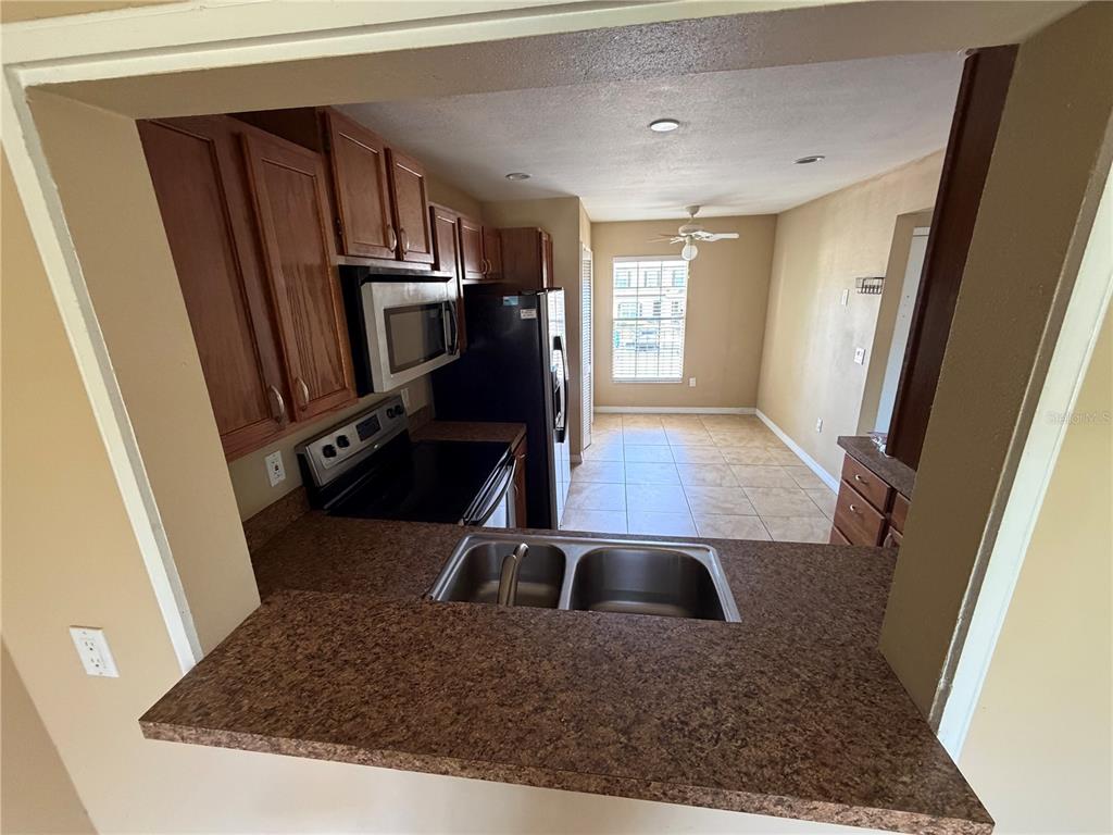 A kitchen with brown cabinets, black appliances, and a pass-through sink overlooking a dining area — 600 NORTHERN WAY UNIT 702, WINTER SPRINGS, FL