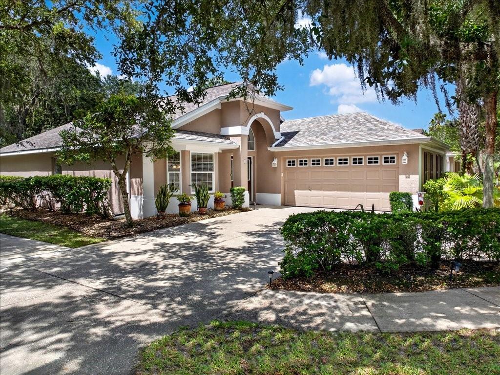A tan single-story house with a two-car garage and a concrete driveway under oak trees — 1 GLENEAGLES PLACE, PALM COAST, FL