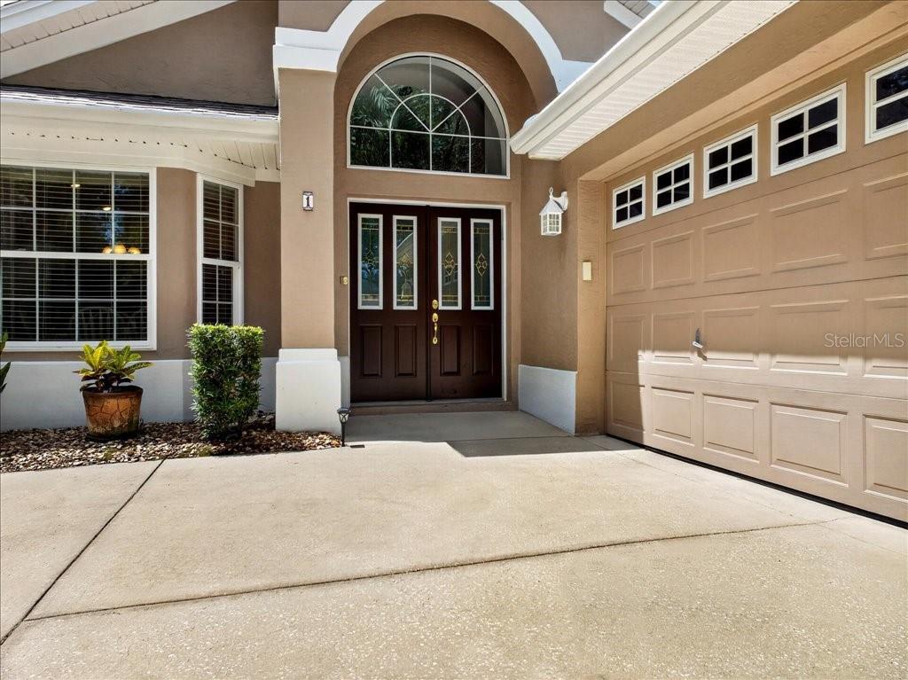 The exterior of a house features a tan stucco facade, double front doors, and a garage — 1 GLENEAGLES PLACE, PALM COAST, FL