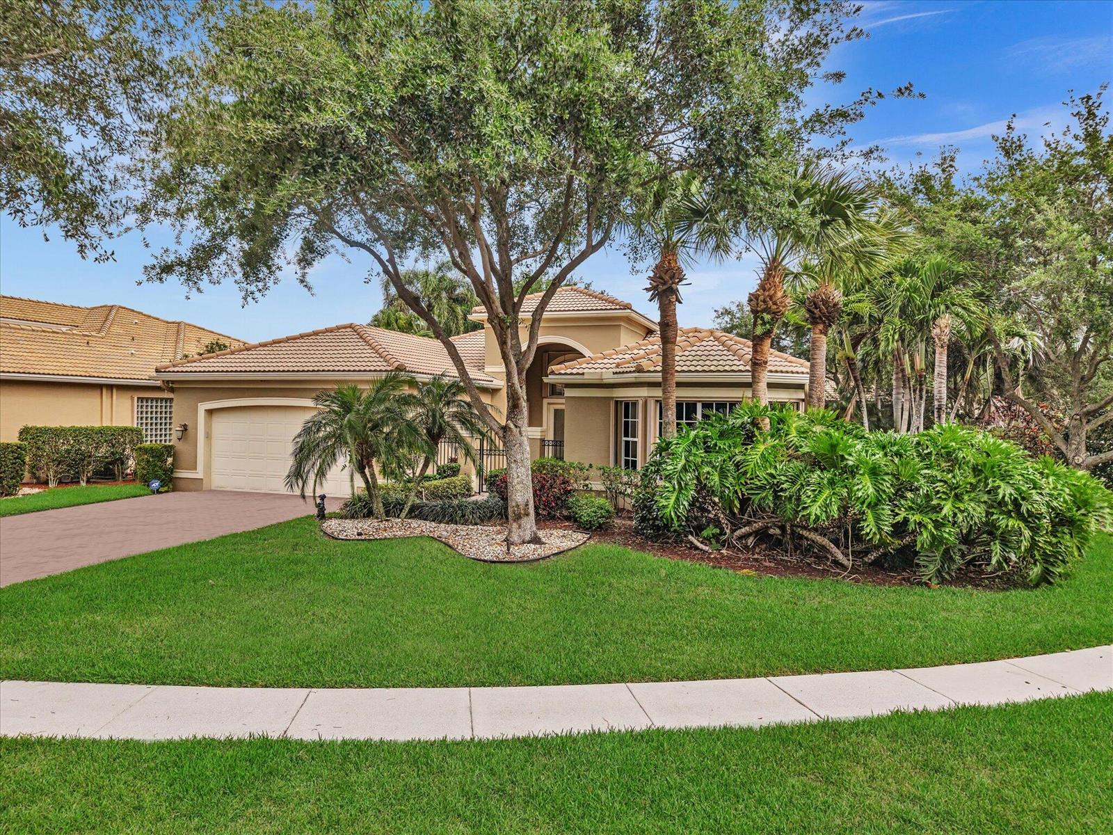 A single-story tan house with a tile roof, two-car garage, and lush tropical landscaping — 7191 Corning Circle, Boynton Beach FL 33437, BOYNTON BEACH, FL