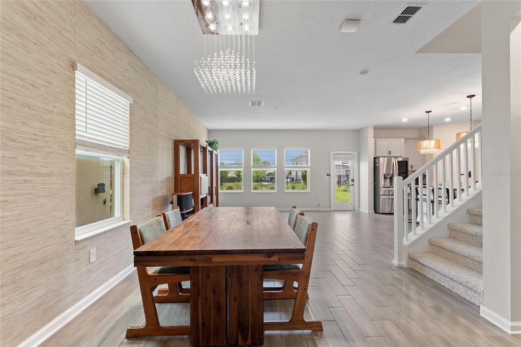 A dining area with a wooden table, chandelier, textured wallpaper, and stairs leading upstairs — 8995 FLUFFY LIE COURT, DAVENPORT, FL